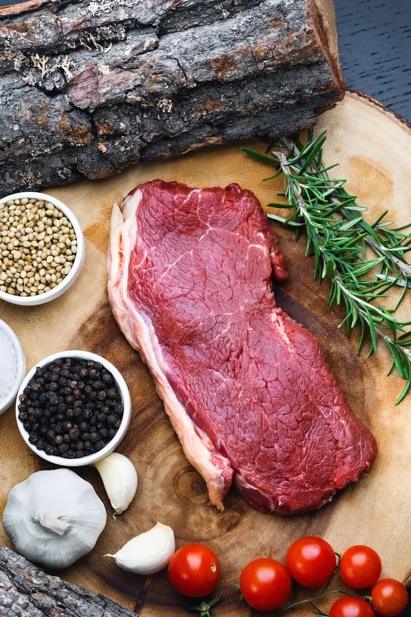 Ein Stück rohes Rindfleisch mit Rosmarin auf einem Holzbrett